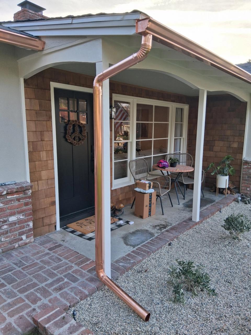 Polished copper downspout and gutter running along a cedar-shingled front porch