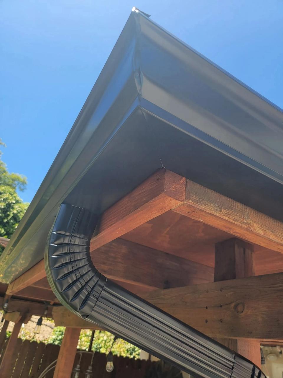Dark bronze gutter and crimped downspout elbow mounted on exposed redwood rafter beams