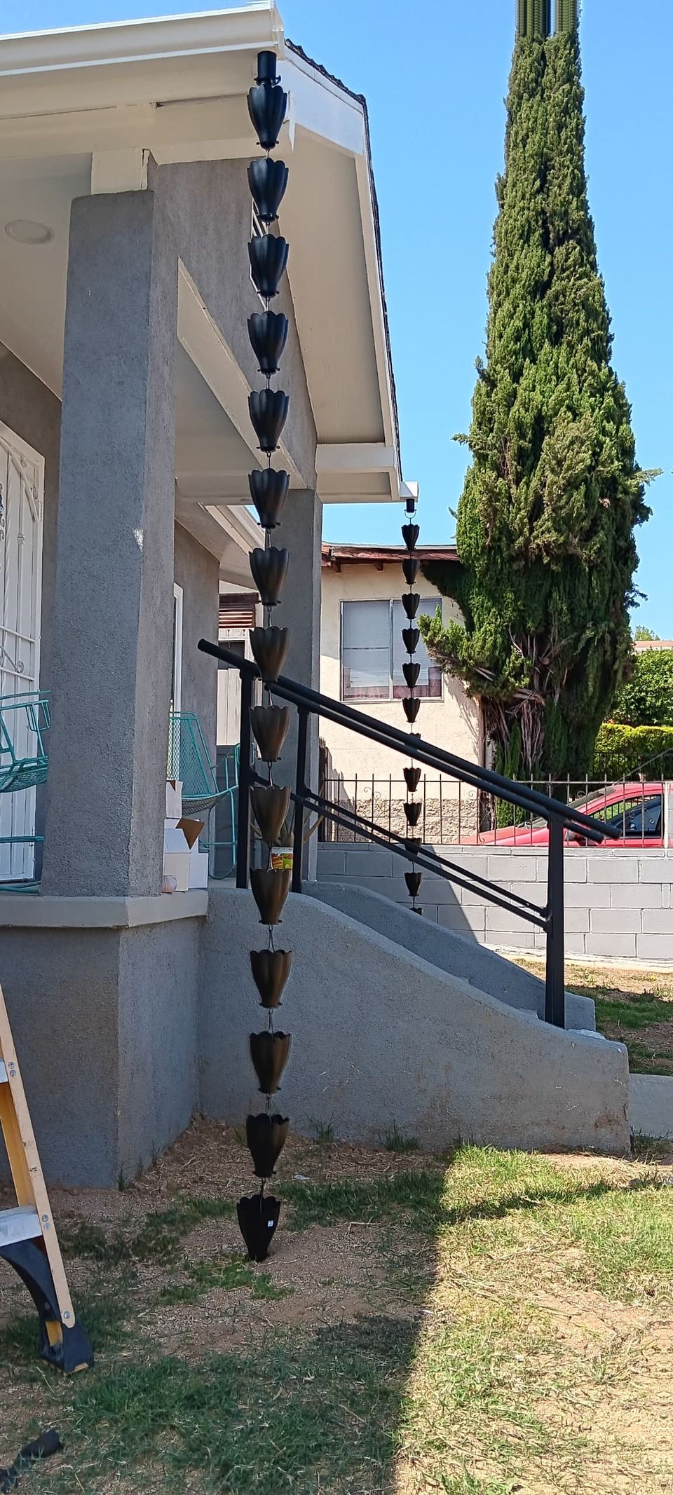 Black cup-style decorative rain chain hanging from a porch gutter in place of a downspout