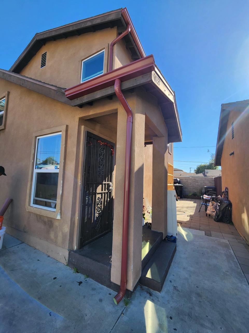 Burgundy gutters and downspout matched to the trim of a two-storey tan stucco home