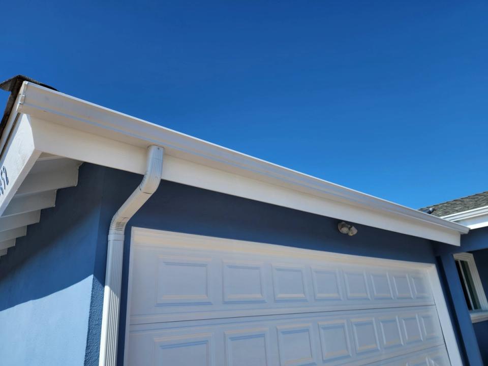White seamless gutter and downspout on a blue-grey house against a deep blue sky