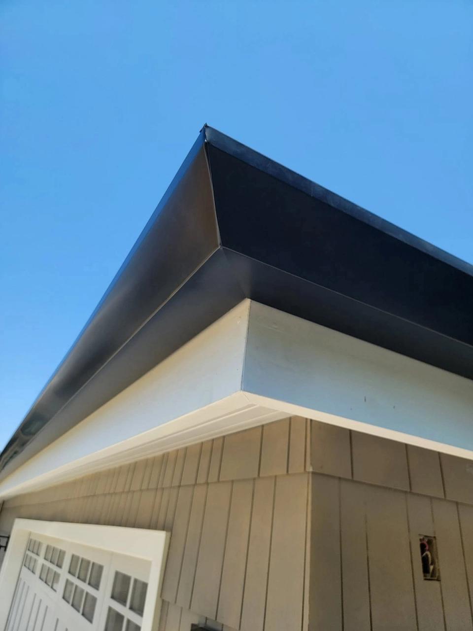 Clean bronze gutter corner miter against a blue sky above tan board-and-batten siding