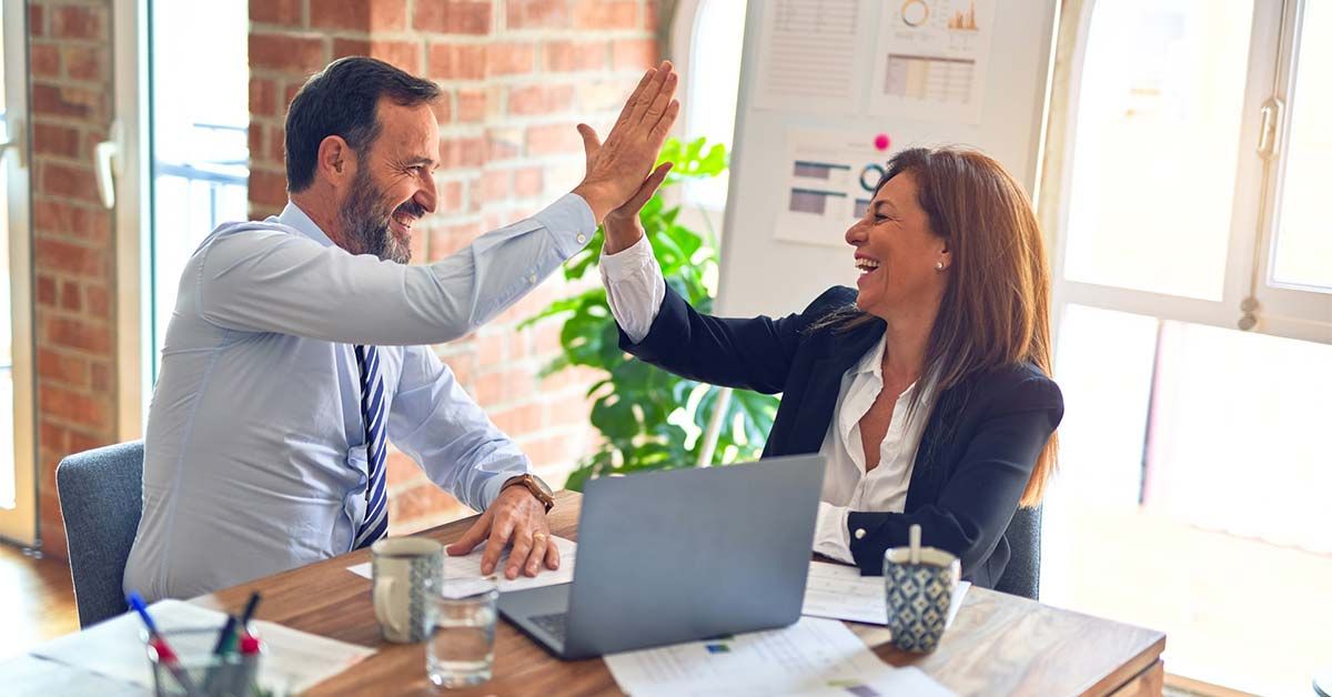 Male and female coworkers high-fiving at desk