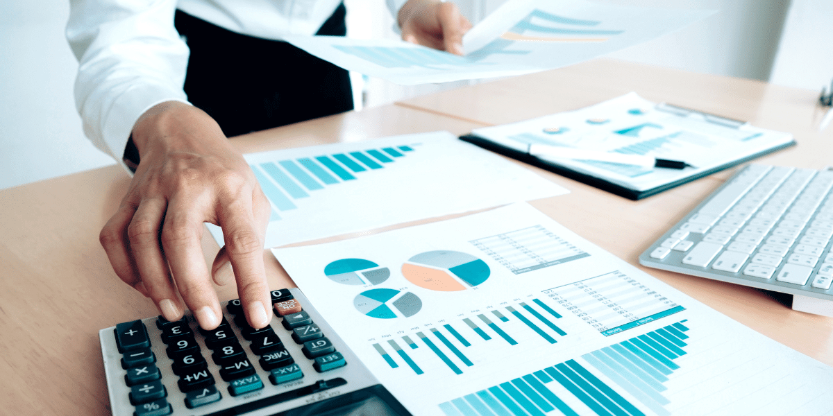 Professional accountant typing on calculator with spreadsheets on desk