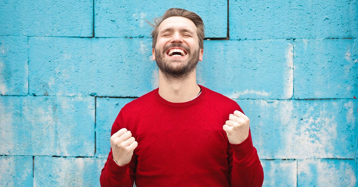 Man in red sweater celebrating by blue brick wall