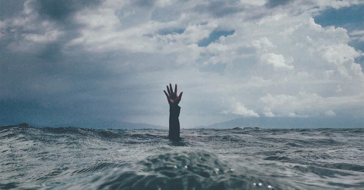 Person under ocean water sticking their hand out to the sky
