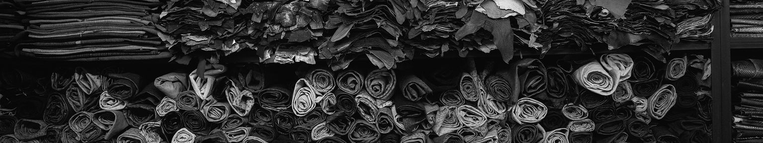 Stacks and rolls of leather or fabric are organized on shelves, with various textures and shades visible in a black and white image.