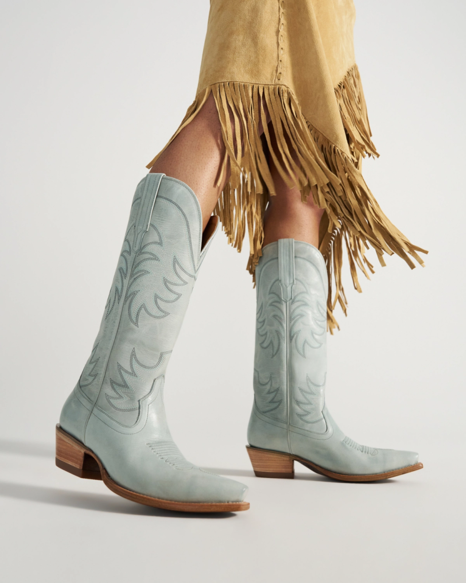The Annie in Slate Blue Cowhide. Person wearing light blue cowboy boots and a tan suede skirt with fringe.