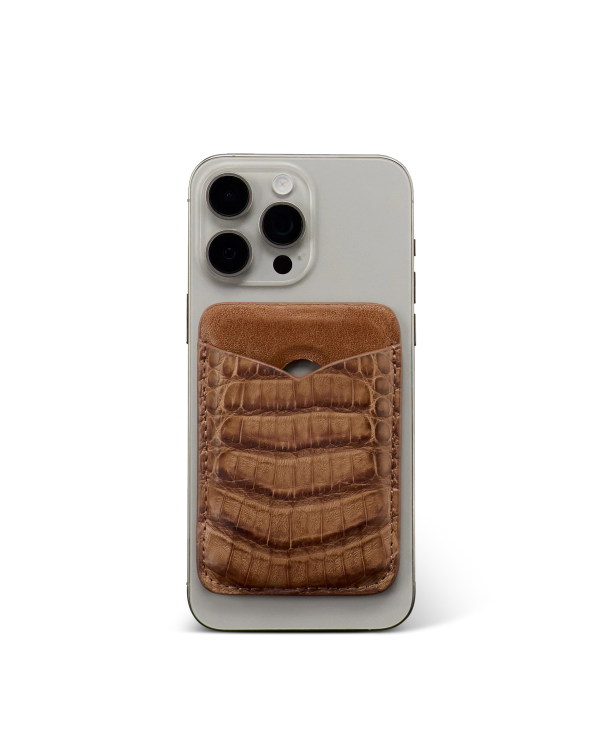 Silver smartphone with a brown, crocodile-patterned leather card holder attached to its back, photographed against a plain white background.
