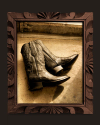 Sepia-toned photo of a pair of cowboy boots resting on a floor, displayed in an ornate wooden frame with carved details.