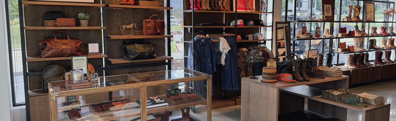 Tecovas Kingston Pike store interior. Displaying boots, hats, and leather goods on shelves and in glass cases, with natural light from large windows and neatly organized merchandise.