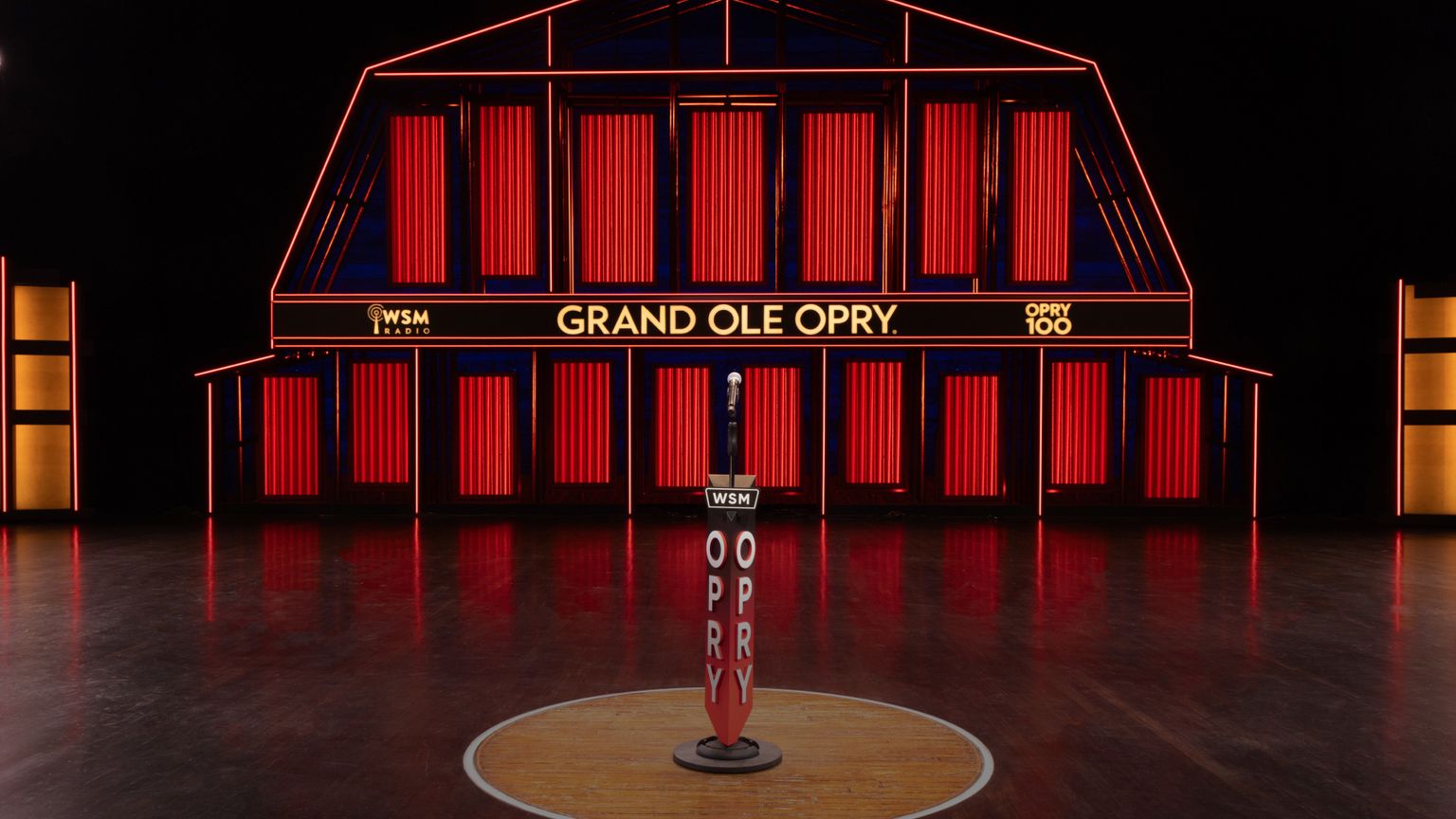 A stage with red vertical lights and a sign reading "Grand Ole Opry," featuring a microphone stand with "WSM" and "OPRY" labels in the center.