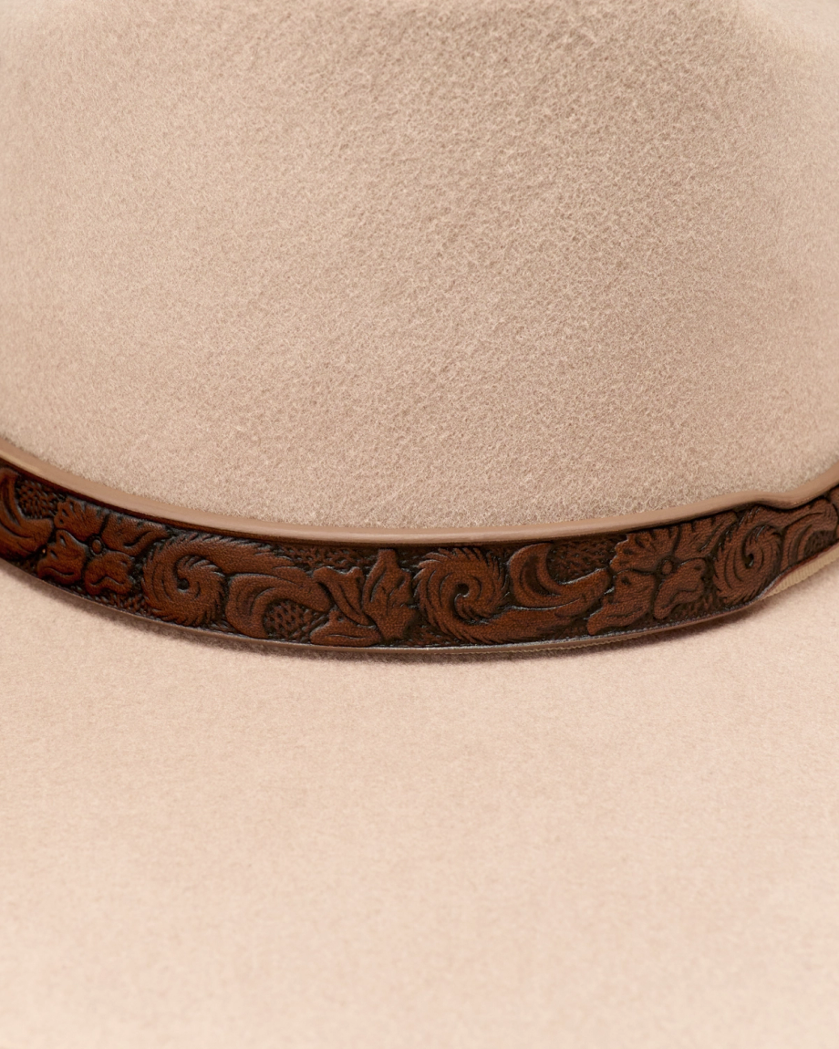 Close-up of a beige felt hat with a brown leather hatband featuring an embossed floral pattern.