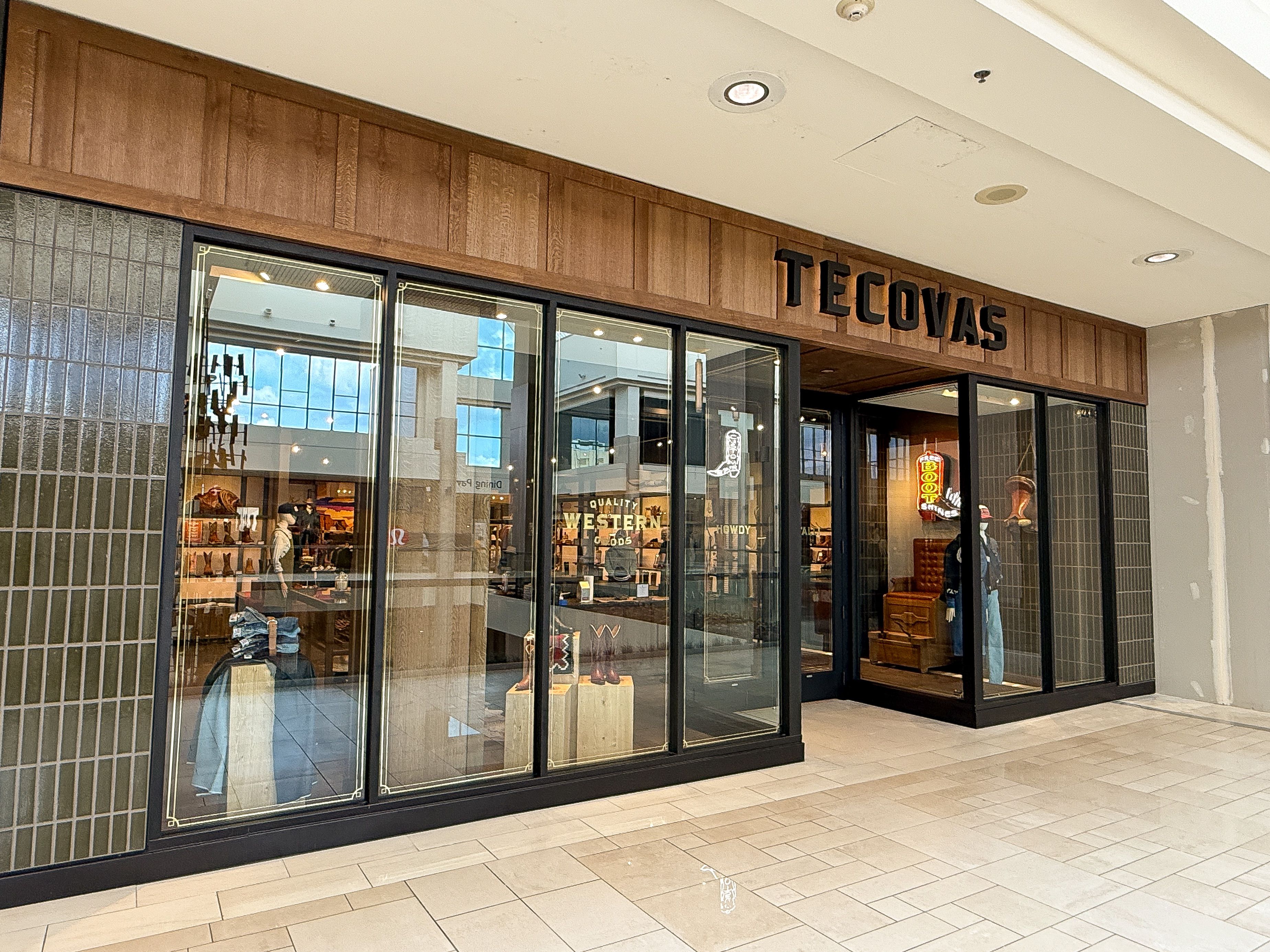 Exterior of a Tecovas store in a shopping mall, showing large glass windows and a wooden sign above the entrance.