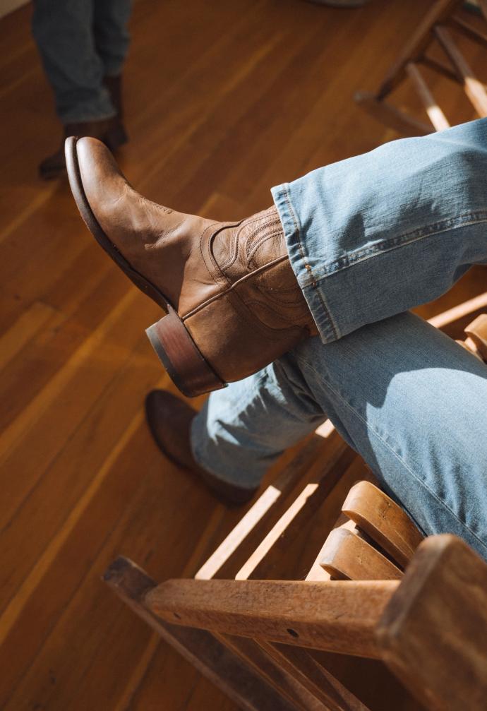 Closeup of man sitting on a wooden rocking chair with the sunlight hitting the boots nicely