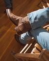 Closeup of man sitting on a wooden rocking chair with the sunlight hitting the boots nicely