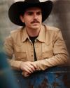 Man in black cowboy hat and tan shirt leaning over truck