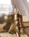 Woman wearing dark brown cafe goat Annie cowgirl boots  standing on a ranch fence