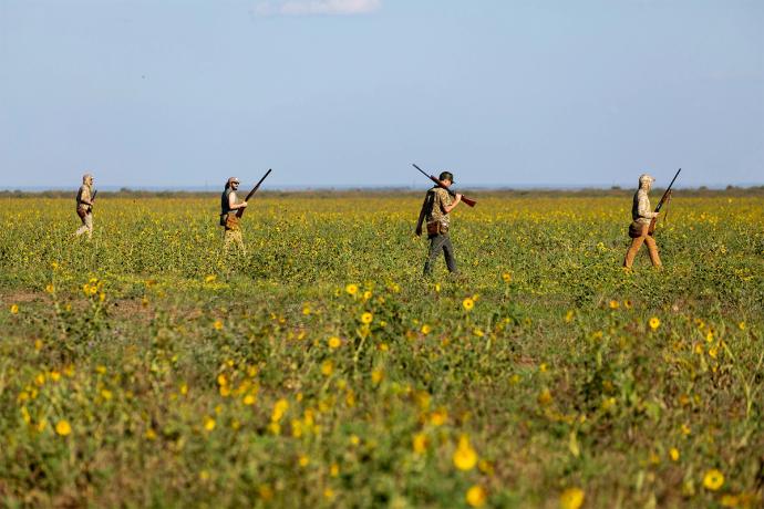 four people in a field with guns