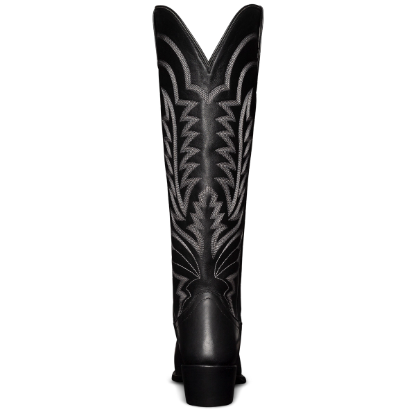 A tall, black cowboy boot with intricate white stitching and a pointed toe, viewed from the front.