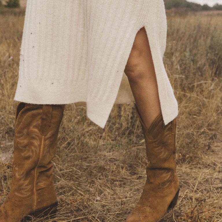 a woman in a field from knees down in a sweater dress and brown suede boots