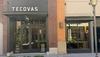 A storefront with a “Tecovas” sign above glass double doors, next to large display windows showing boots inside. Brick and beige building exterior, with a streetlamp and shrubs in front.