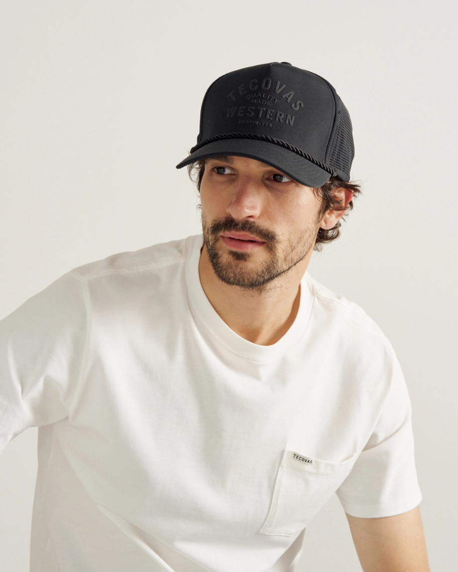 A man with a beard wears a black cap with "Tecovas Quality Made Western" text 