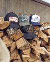 Four tecovas-branded baseball caps on a stack of firewood, featuring various designs and colors.