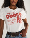 A woman wearing a white T-shirt with red text and graphics that read "Tecovas Rodeo, Bringin' the Wild West to You!" She is also wearing blue jeans and a brown belt.