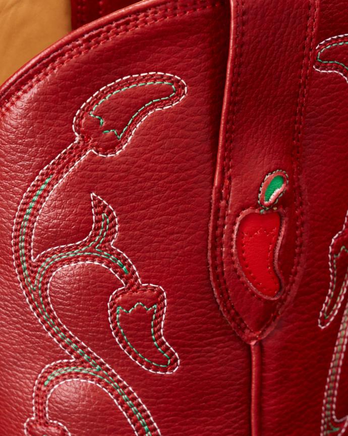 Close-up of red leather with white and green stitching, featuring chili pepper designs and a textured surface.