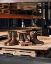 Three pairs of boots displayed on wooden pallets in a warehouse setting.