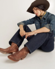 Person wearing a cowboy hat, denim shirt, jeans, and brown cowboy boots sits on the floor with eyes closed and head tilted down.