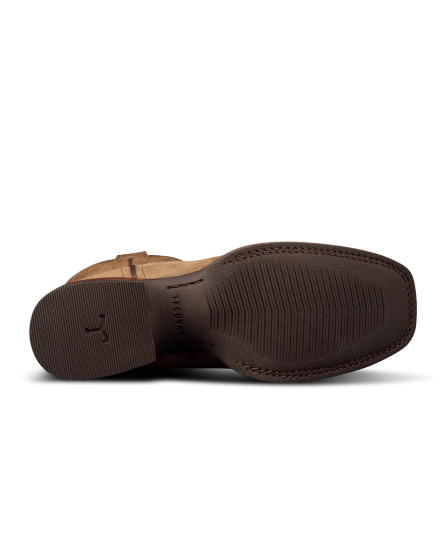 The image shows the bottom view of a brown dress shoe with visible textured grip patterns and a small logo near the heel, resembling styles found at The Tess Goat Cafe.