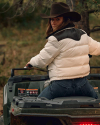 A person in a cowboy hat and white jacket sits on an ATV, looking back. They are outdoors with trees in the background.