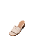 The Carmen Paloma in Pearl Ostrich. A beige open-toe heeled slide sandal, The Carmen Paloma Ostrich, features a wide textured strap and a low wooden block heel, displayed on a plain white background.