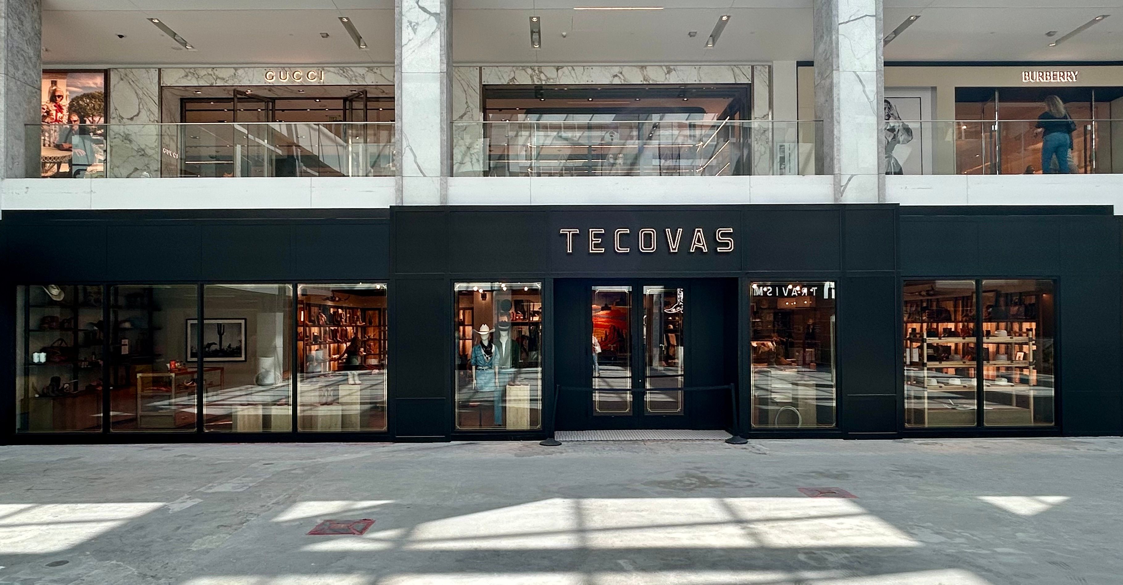 Front view of a Tecovas store in a shopping mall, with glass doors and windows, and Gucci and Burberry stores visible on the upper level.