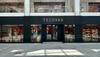 Front view of a Tecovas store in a shopping mall, with glass doors and windows, and Gucci and Burberry stores visible on the upper level.