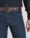 A person wearing blue jeans, a brown leather belt with a brass buckle, and a black long-sleeve shirt.