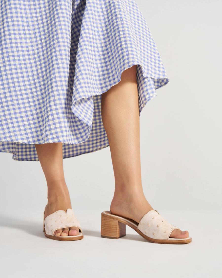 A person wearing a blue and white gingham skirt and beige heeled sandals stands against a plain background, showcasing the elegance of The Carmen Paloma Ostrich Pearl handbag.