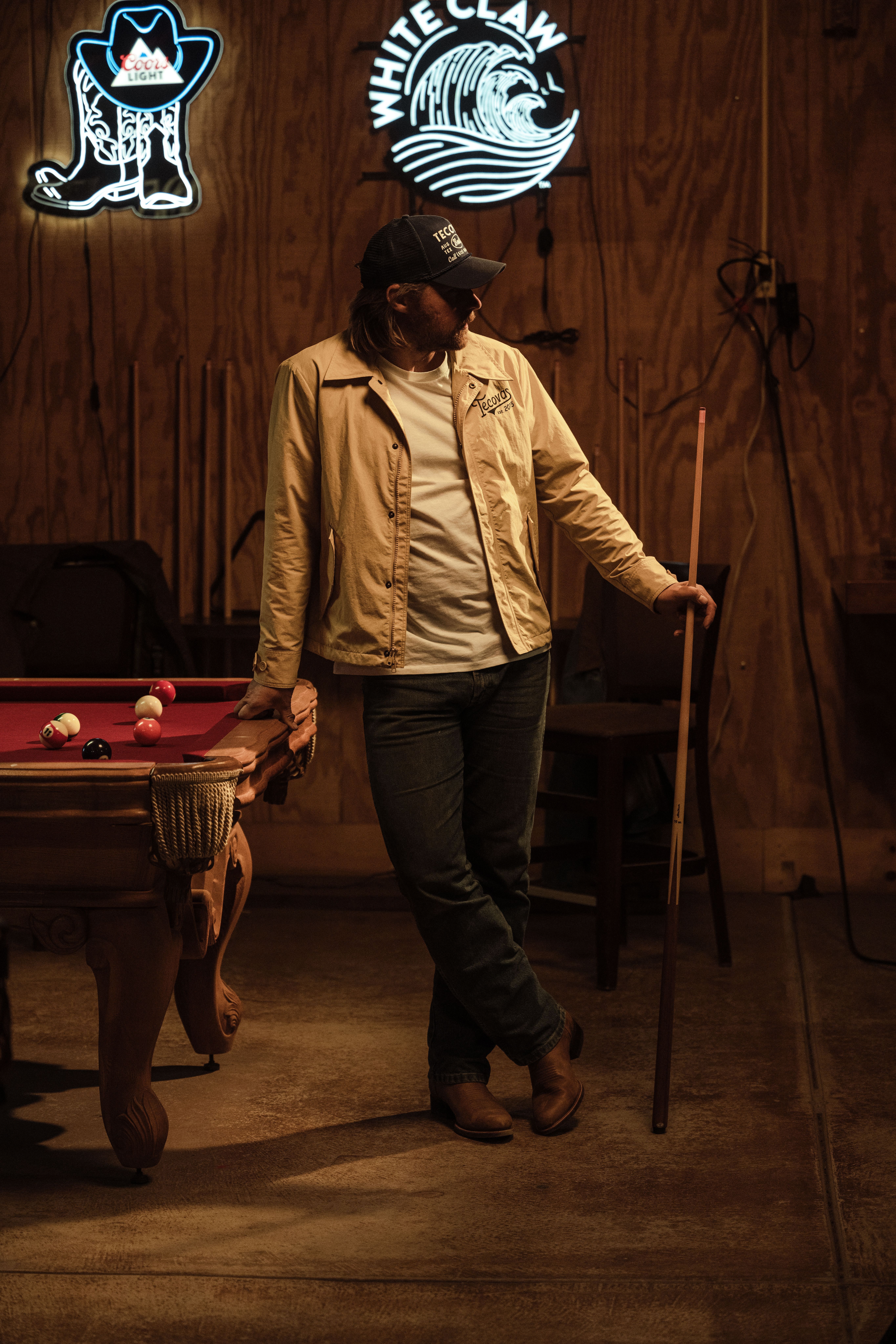 Man wearing a Tecovas blue pearl snap and cowboy hat adjusts the bridle on a horse.