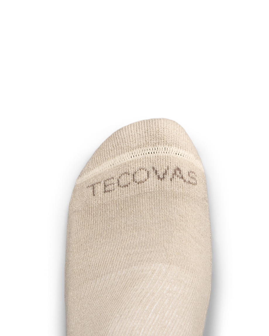 Close-up of the toe of a beige sock with the word "TECOVAS" stitched in brown letters near the seam, shown on a white background.