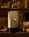 An old metal safe with its door open sits on a shelf surrounded by framed art, antlers, books, and rustic decor items.