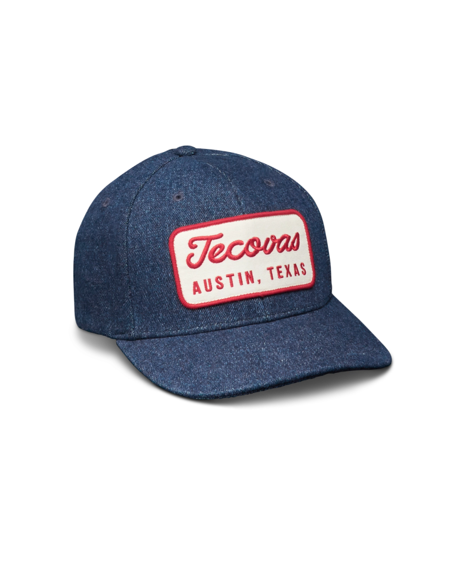 A blue denim baseball cap with a red and white patch on the front that reads "Tecovas Austin, Texas.