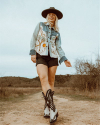 Woman in denim jacket and cowboy boots walking on a dirt path.