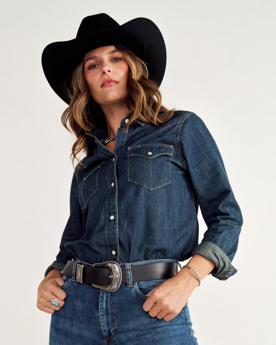 Person in a denim outfit wearing a black cowboy hat and a belt with a decorative buckle.