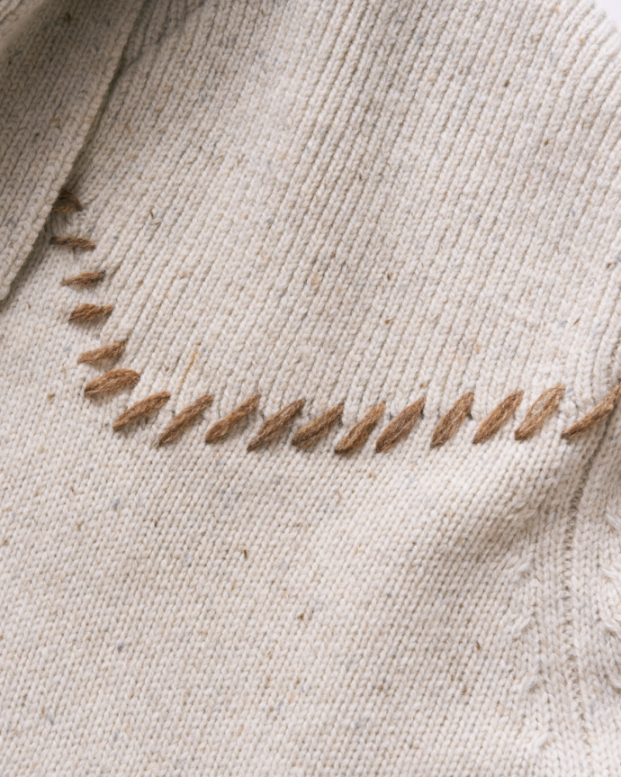 Close-up of a beige knitted fabric with brown zigzag stitching near the collar.