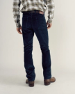 A person stands facing away, wearing a plaid shirt, dark jeans, a brown belt, and brown boots against a plain background.