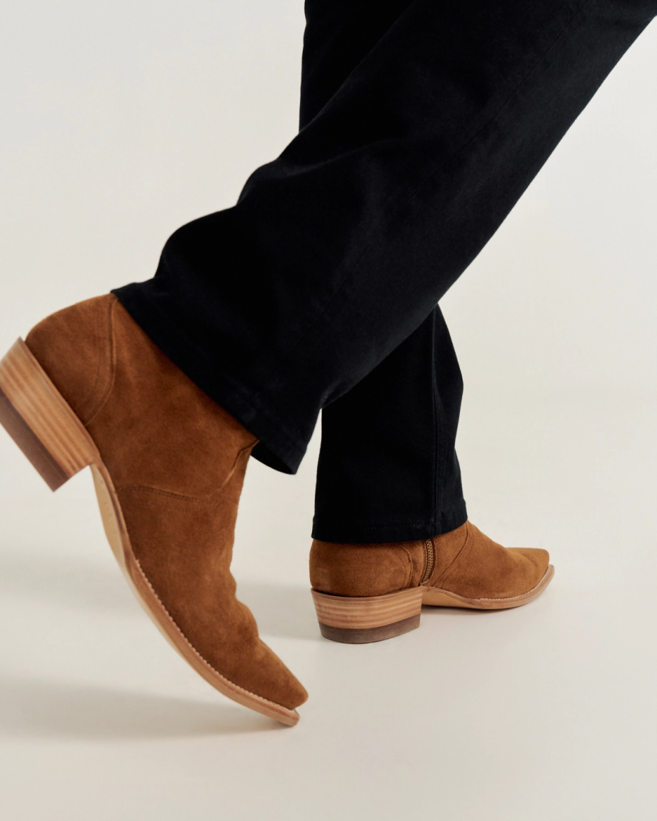 Person wearing brown suede ankle boots with wooden heels and black pants.