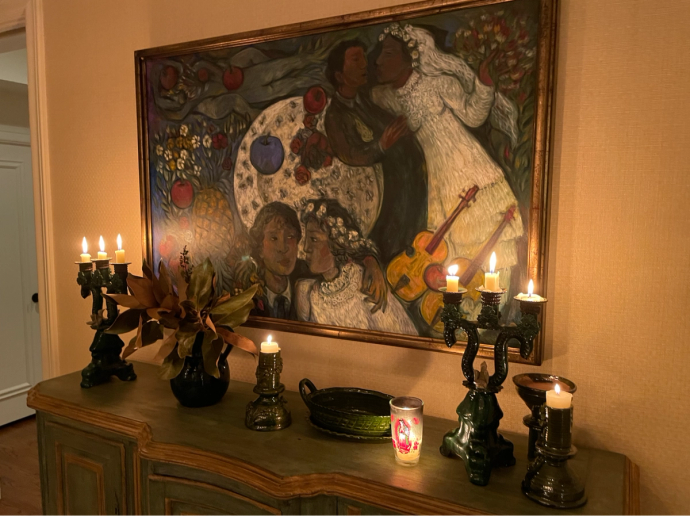 An image of a beautiful painting framed on the wall above a credenza with lit candles.