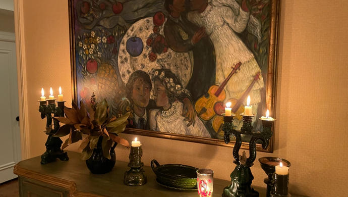 An image of a beautiful painting framed on the wall above a credenza with lit candles.